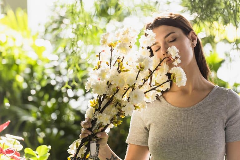 attractive woman holding bunch flower twigs near face min scaled